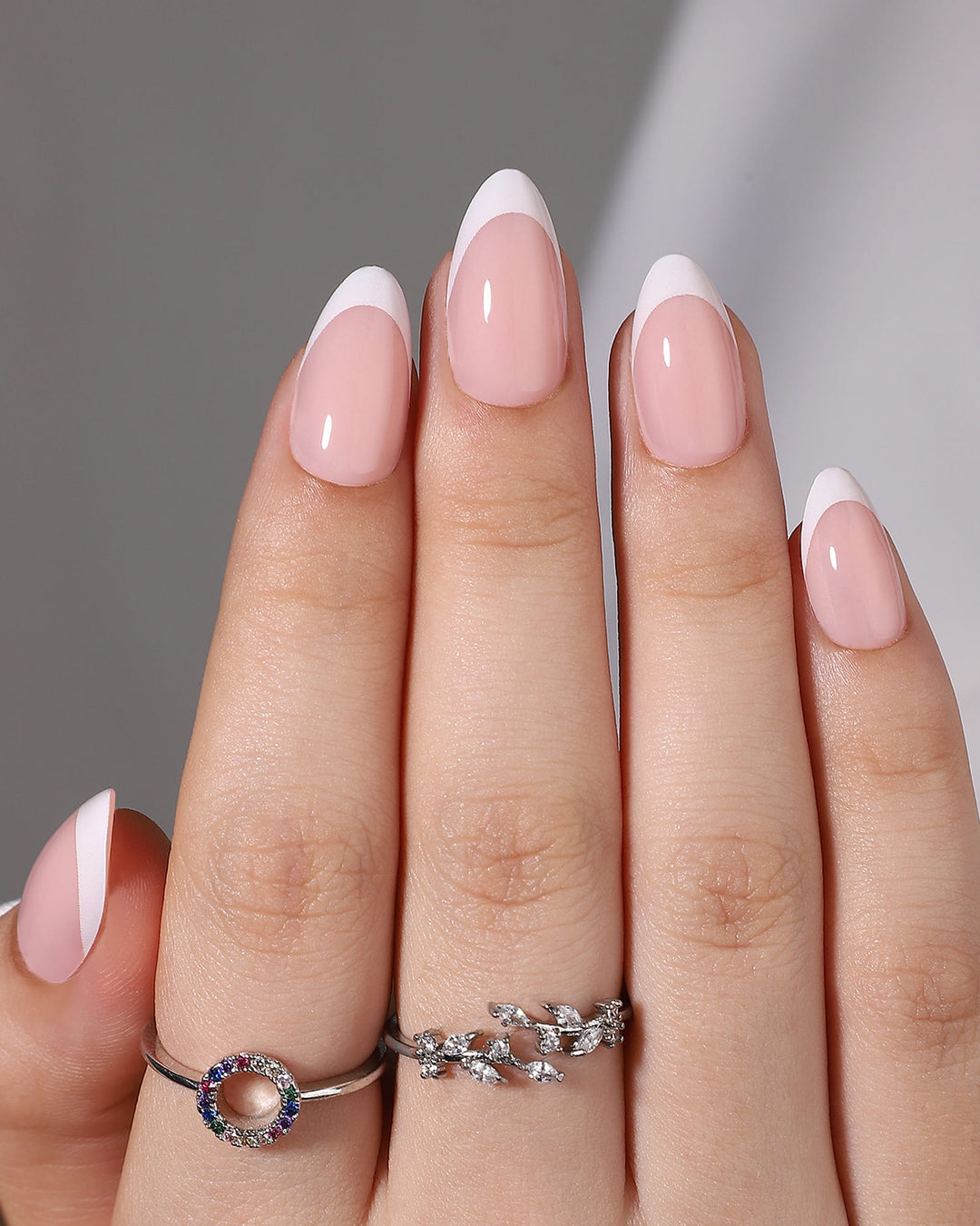 Close-up of a hand with pink and white nail polish wearing two silver rings.